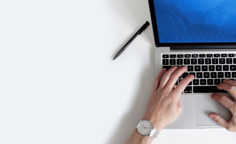 Person wearing watch typing on a laptop with pen on the side