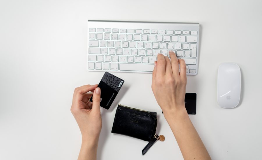 person typing on computer keyboard with right hand while holding a black visa card on left hand