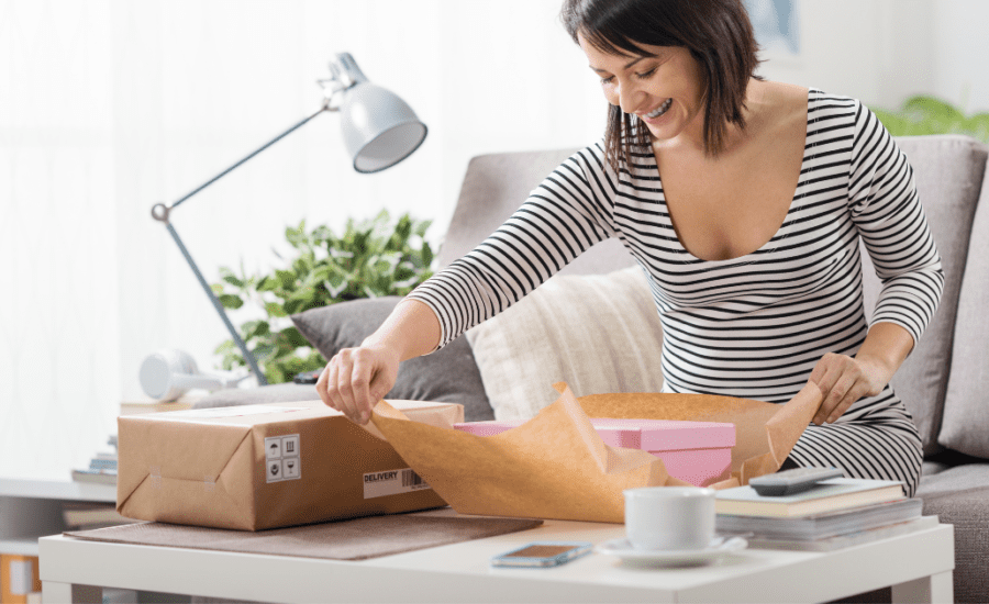 Woman wrapping a pink box with brown kraft paper, white coffee cup on the table and white table lamp